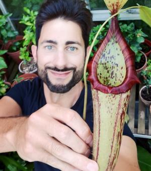 Chris Thorogood holding a flower, smiling at the camera, they have dark hair and are wearing a black t shirt