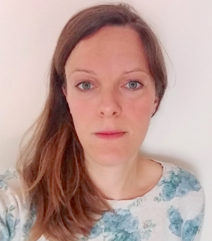 Olivia Smith looking directly at the camera, They have long brown hair and are wearing a blue top