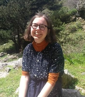 Rachel Hindmarsh, a woman with short hair and glasses, smiles in front of a greenspace