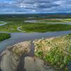 Aerial landscape photo of the Y-K Delta, showing a lush green tundra landscape dappled with lakes and rivers. There is a mountain range in the background.