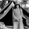 black and white photograph (1909) of woman standing in front of a tent, palm trees behind her