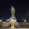 Nighttime image of bronze statue of a man standing on the top of an orb